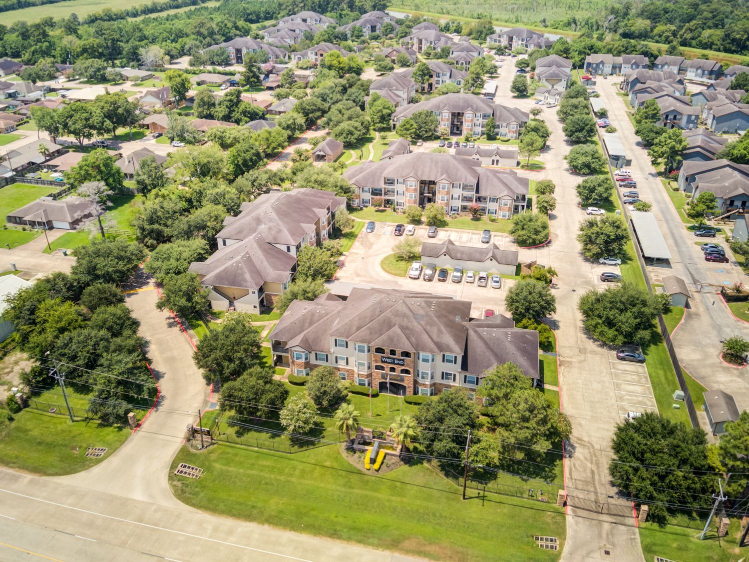 Aerial view of an apartment complex with multiple buildings, trees, and a playground in a green area.