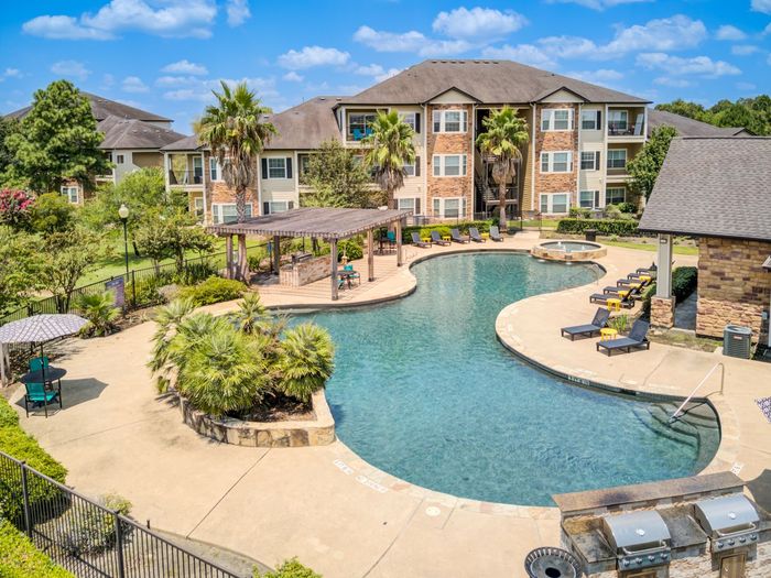 Apartment complex with a large, winding pool, lounge chairs, and a pergola.