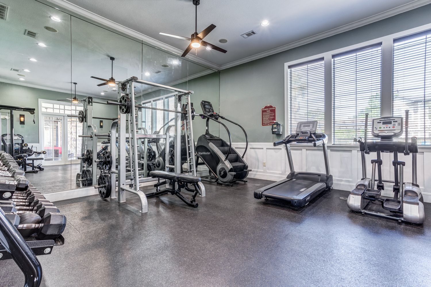Gym with weights, machines, and treadmills; large mirror; black rubber floor.