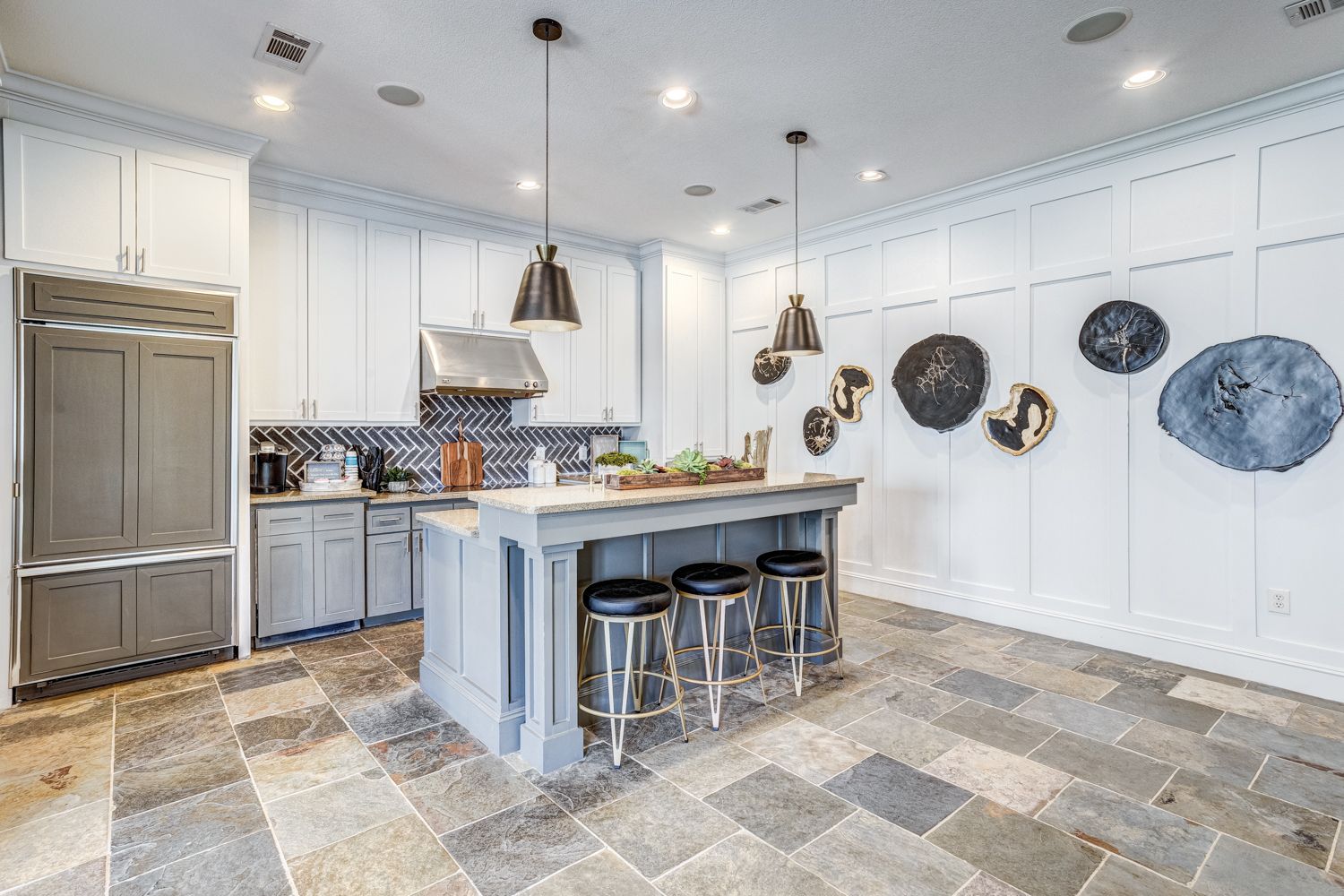 Gray and white kitchen with island, stools, stone floor, and wall art.