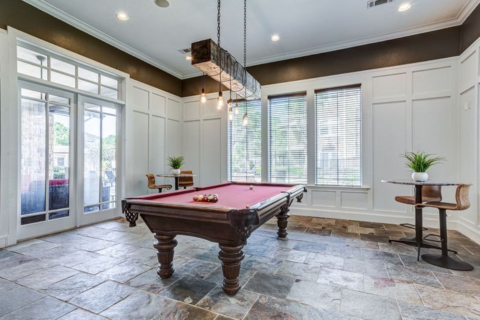 Pool table in a room with large windows and rustic flooring.
