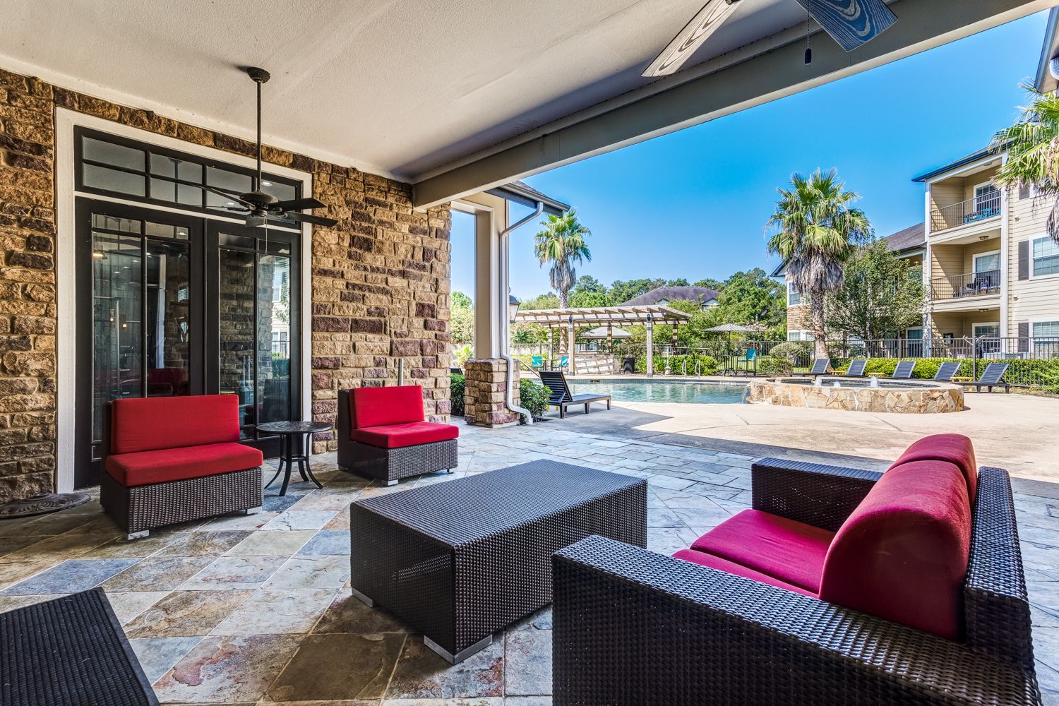 Patio with red furniture, stone walls, overlooking a pool area. Sunny day.