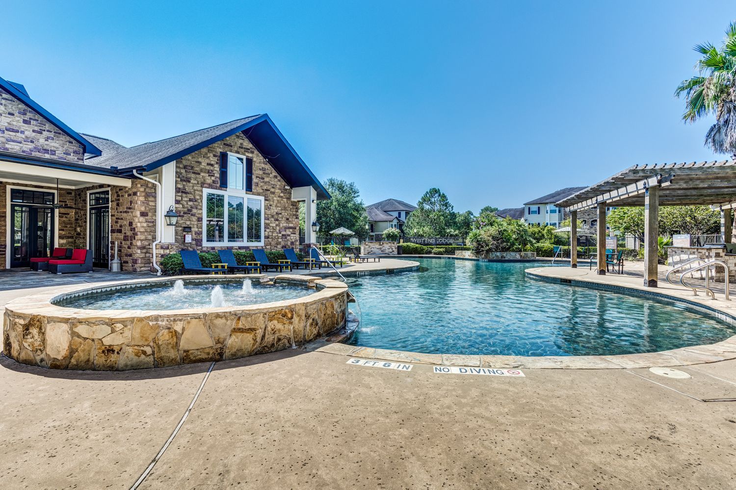 Swimming pool and stone fountain in front of a brick building on a sunny day.
