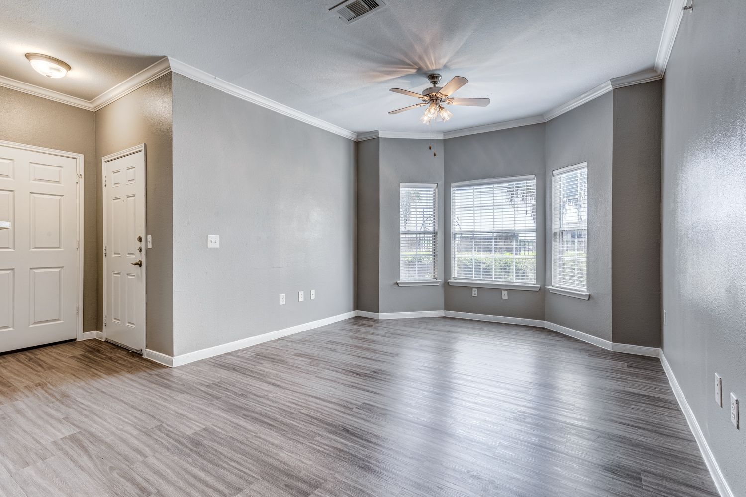 Empty living room with gray walls, wood-look floor, and bay windows.