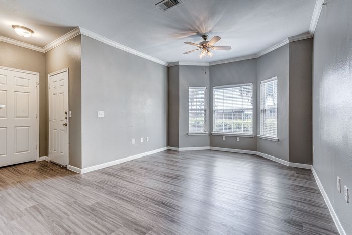 Empty living room with gray walls, wood-look floor, and bay windows.