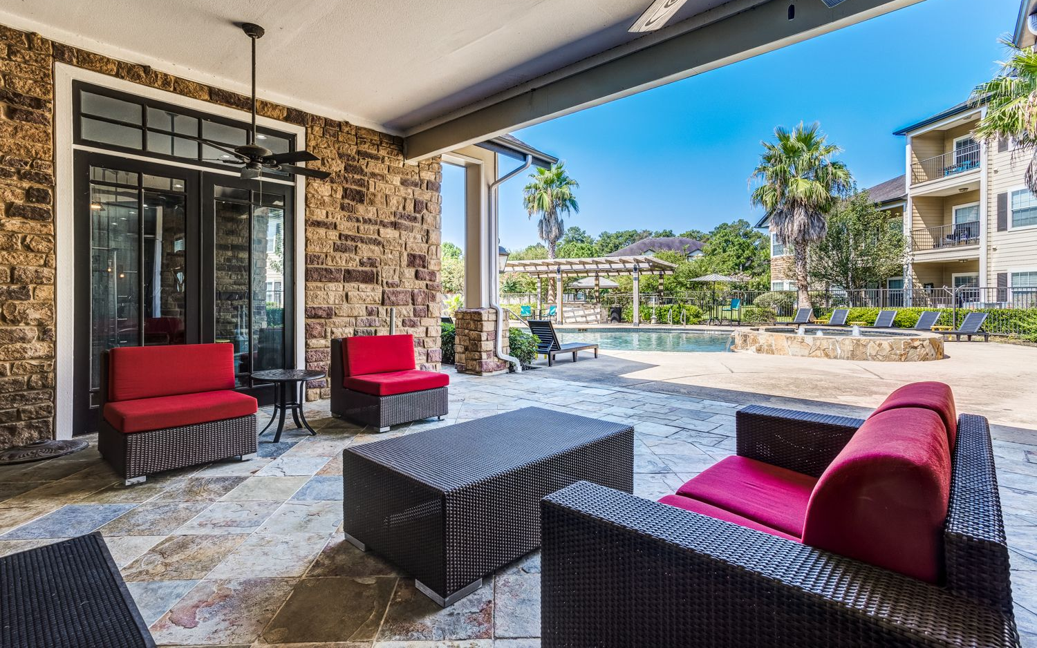 Patio with red furniture, stone walls, overlooking a pool area. Sunny day.