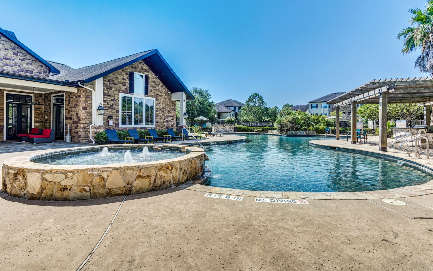 Swimming pool and stone fountain in front of a brick building on a sunny day.