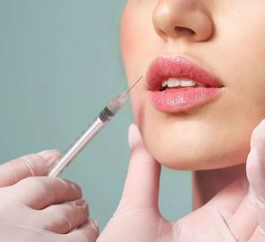 Gloved hands injecting filler into a woman’s lips with a syringe in close-up