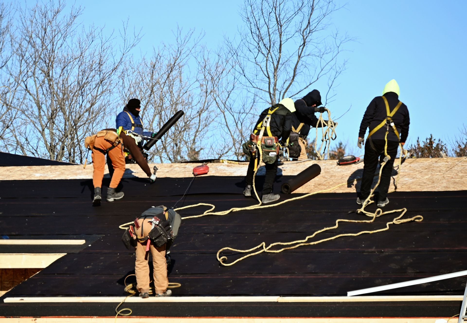 six men performing roofing repairs on a house, using tools and safety gear for maintenance work.