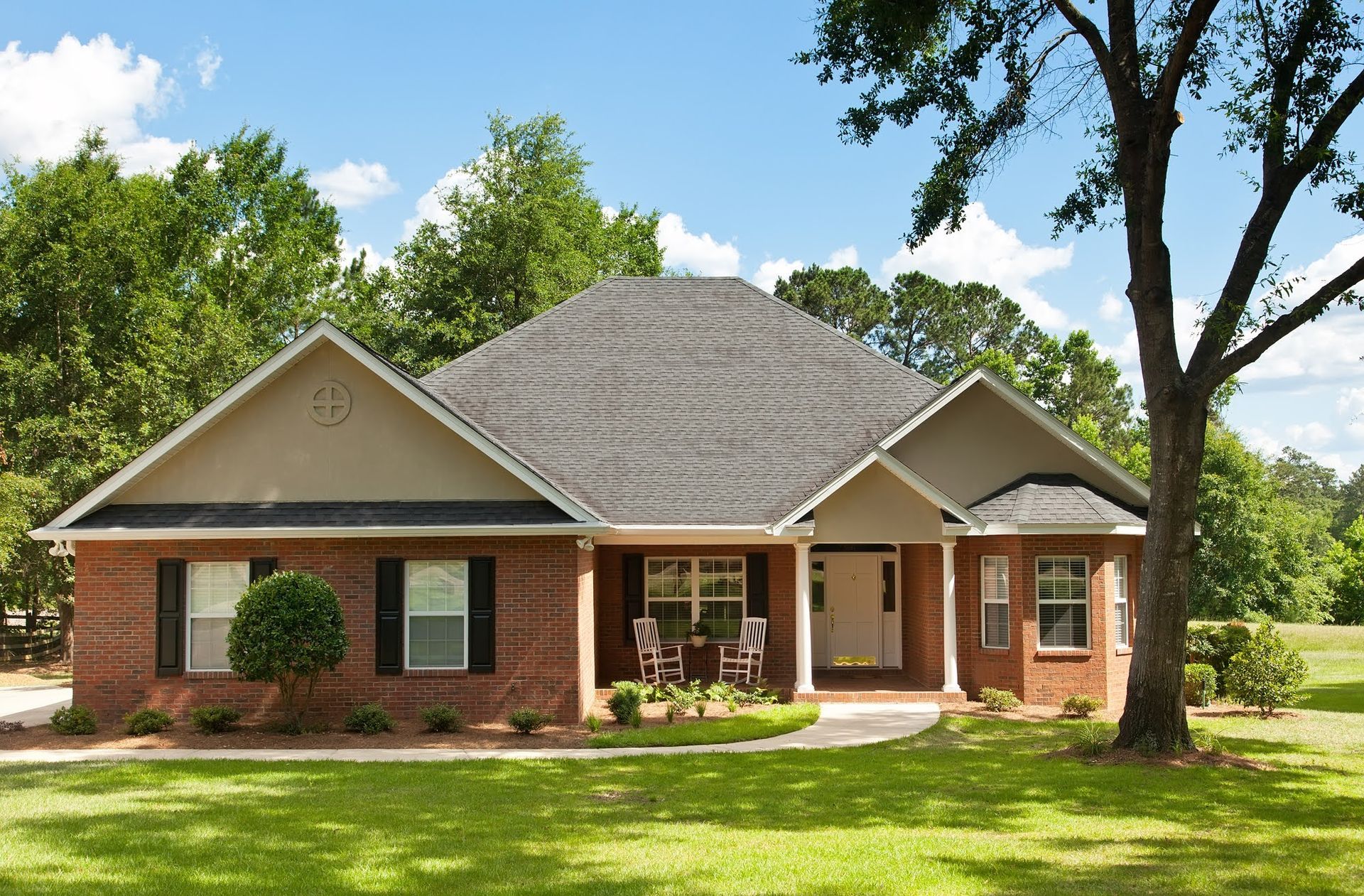 A brick house with a porch and a tree in front of it