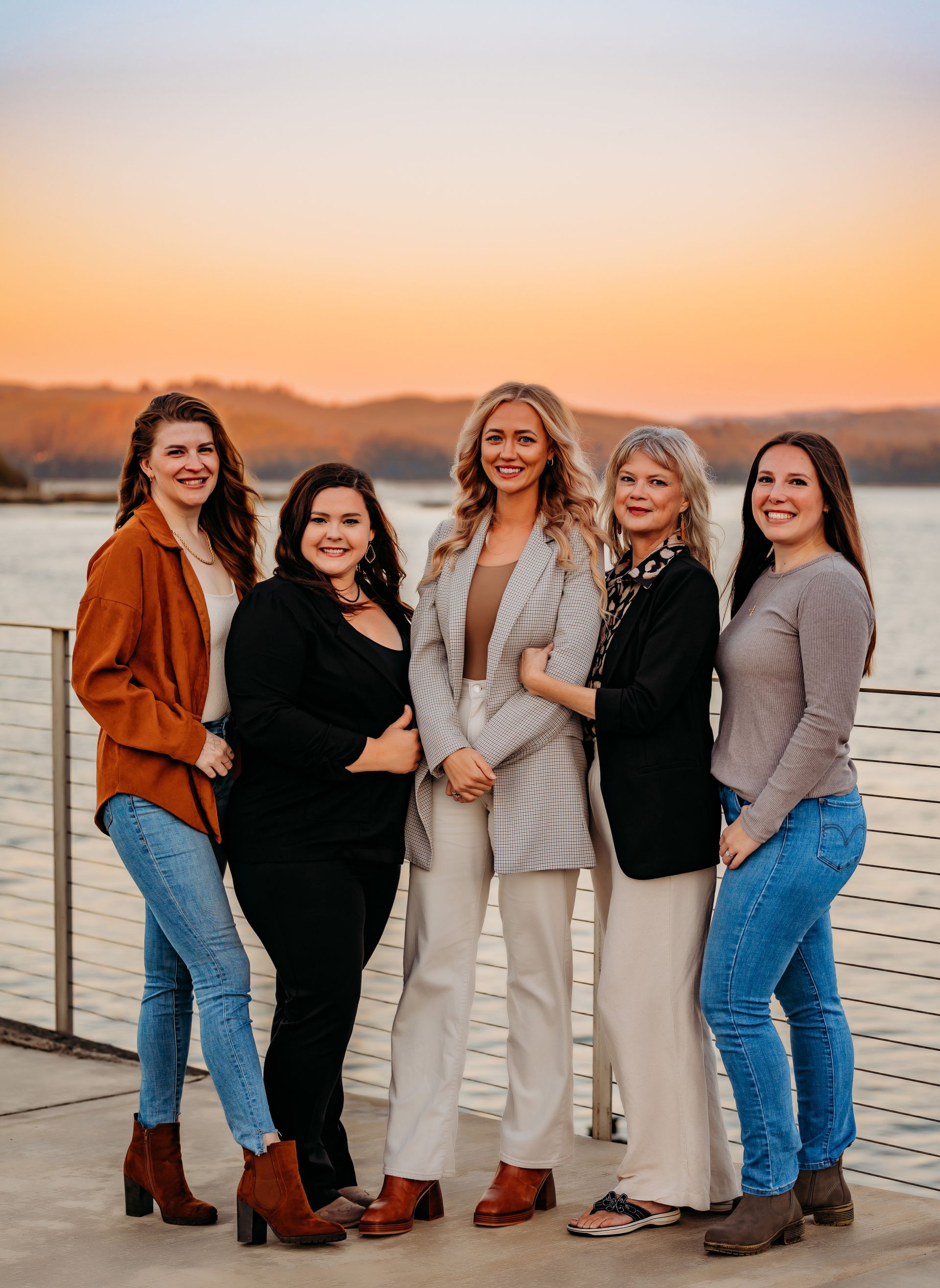 A group of women are posing for a picture in front of a body of water