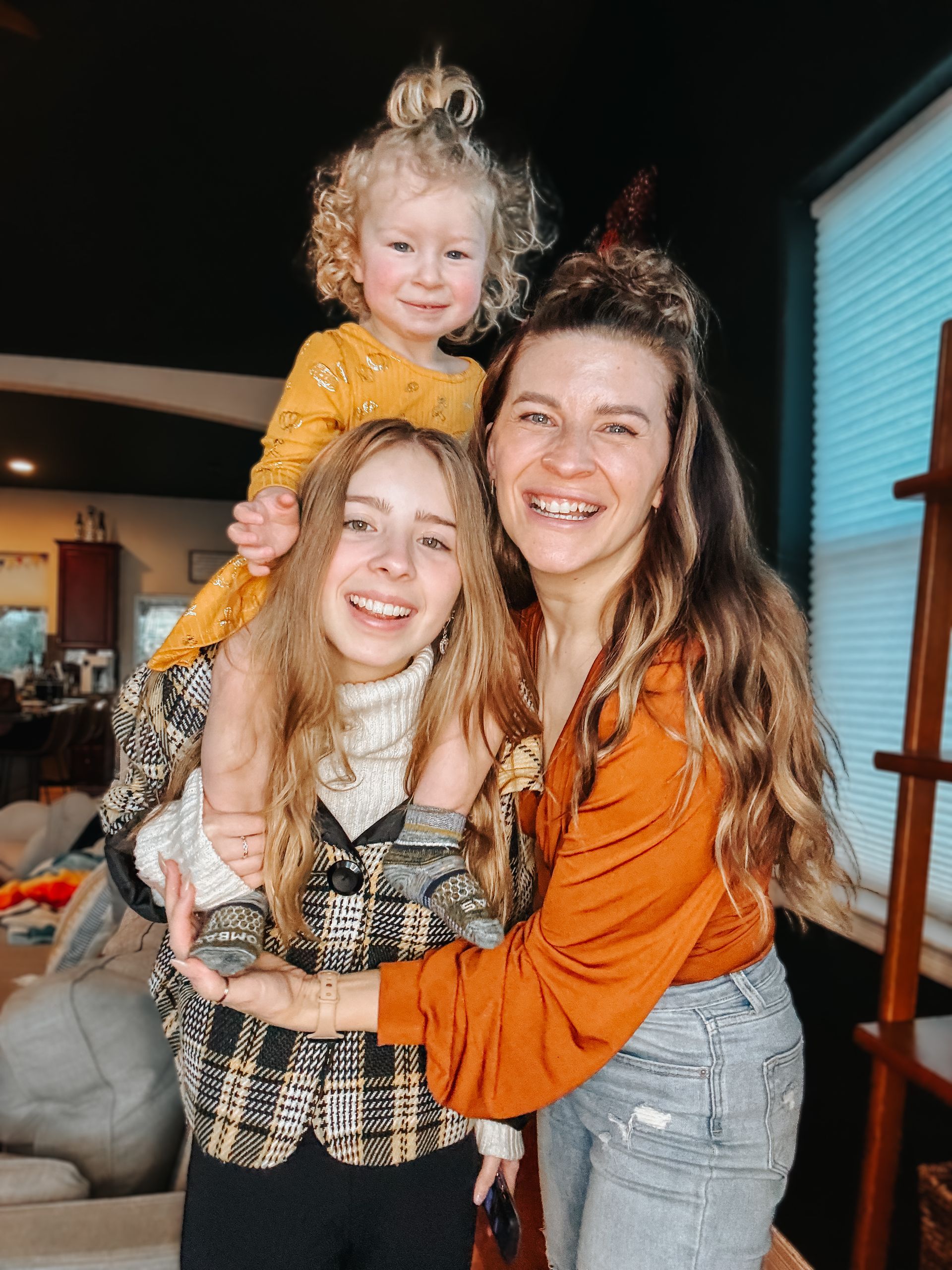 A woman is holding a little girl on her shoulders in a living room.