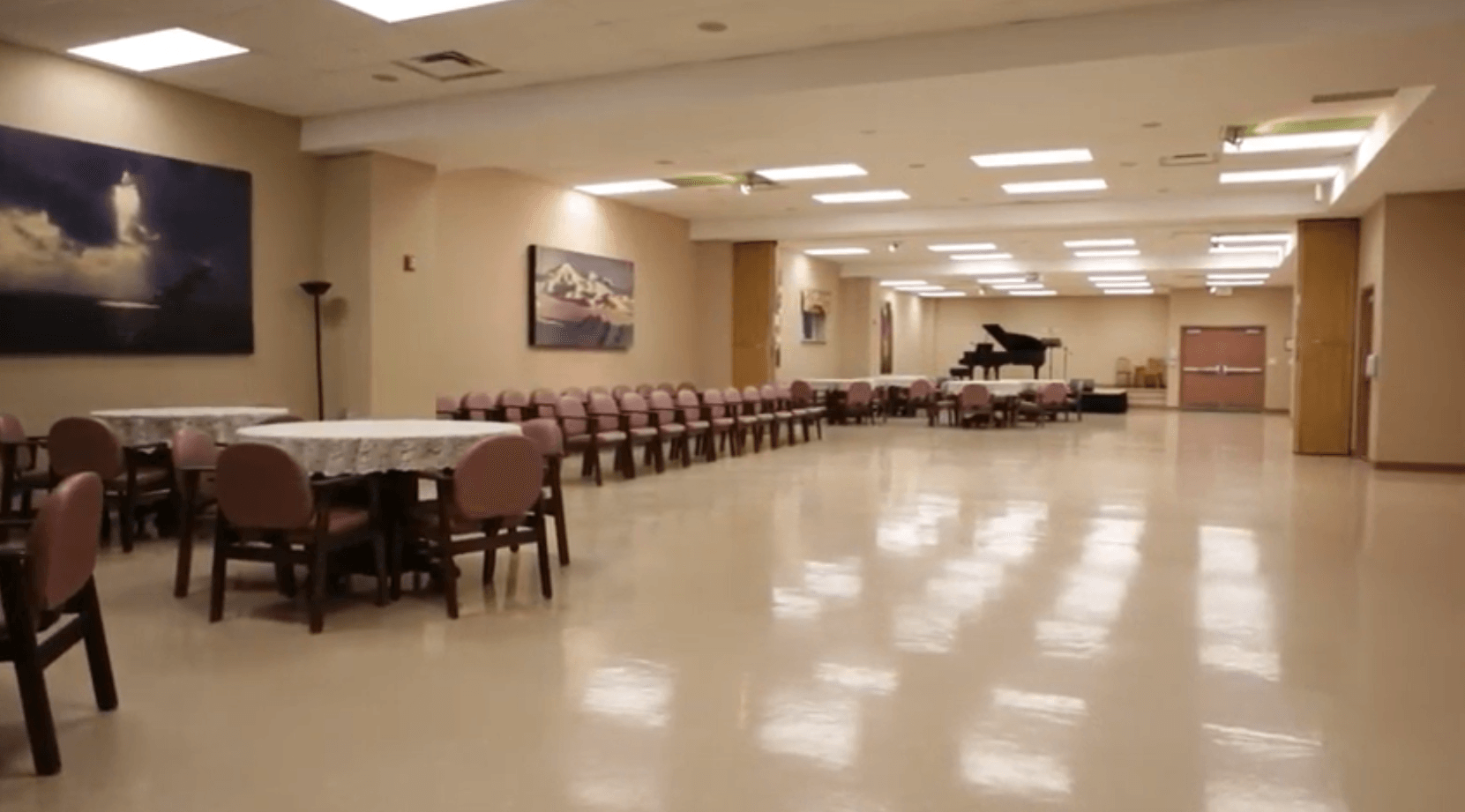A large room with tables and chairs and a piano in Hillcrest Village Long-Term Care Facility