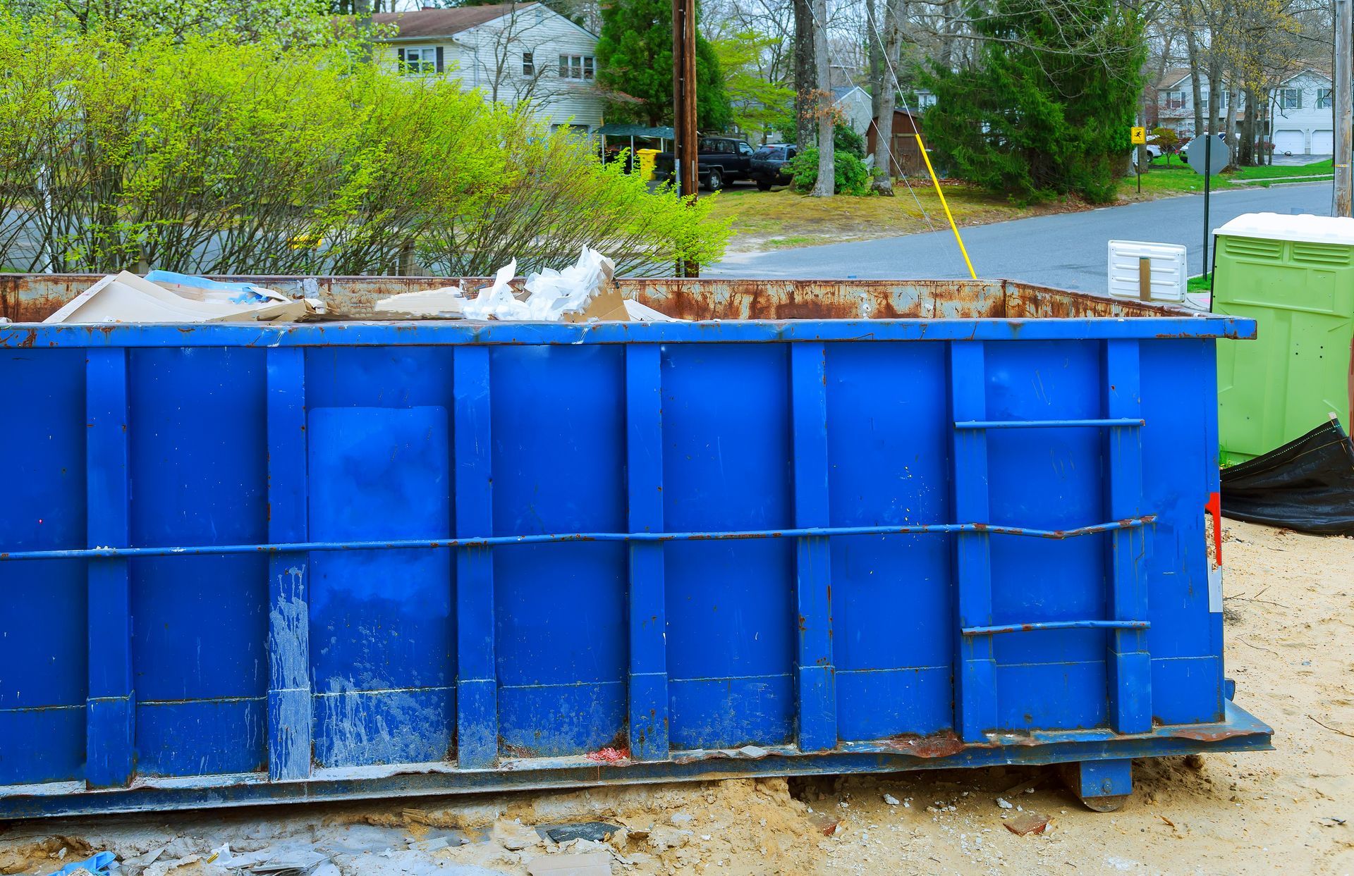 A blue dumpster is sitting on the side of the road.