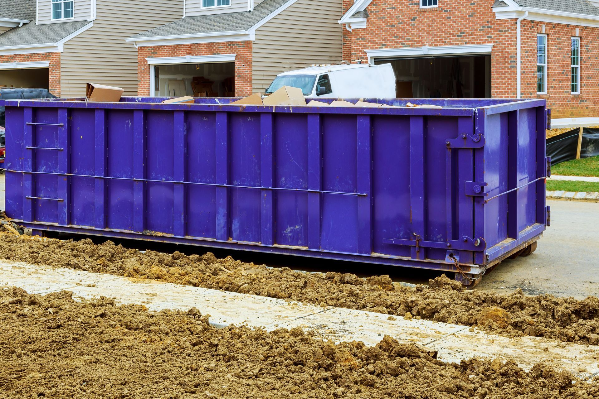 Purple dumpster on a street with construction site in the background.