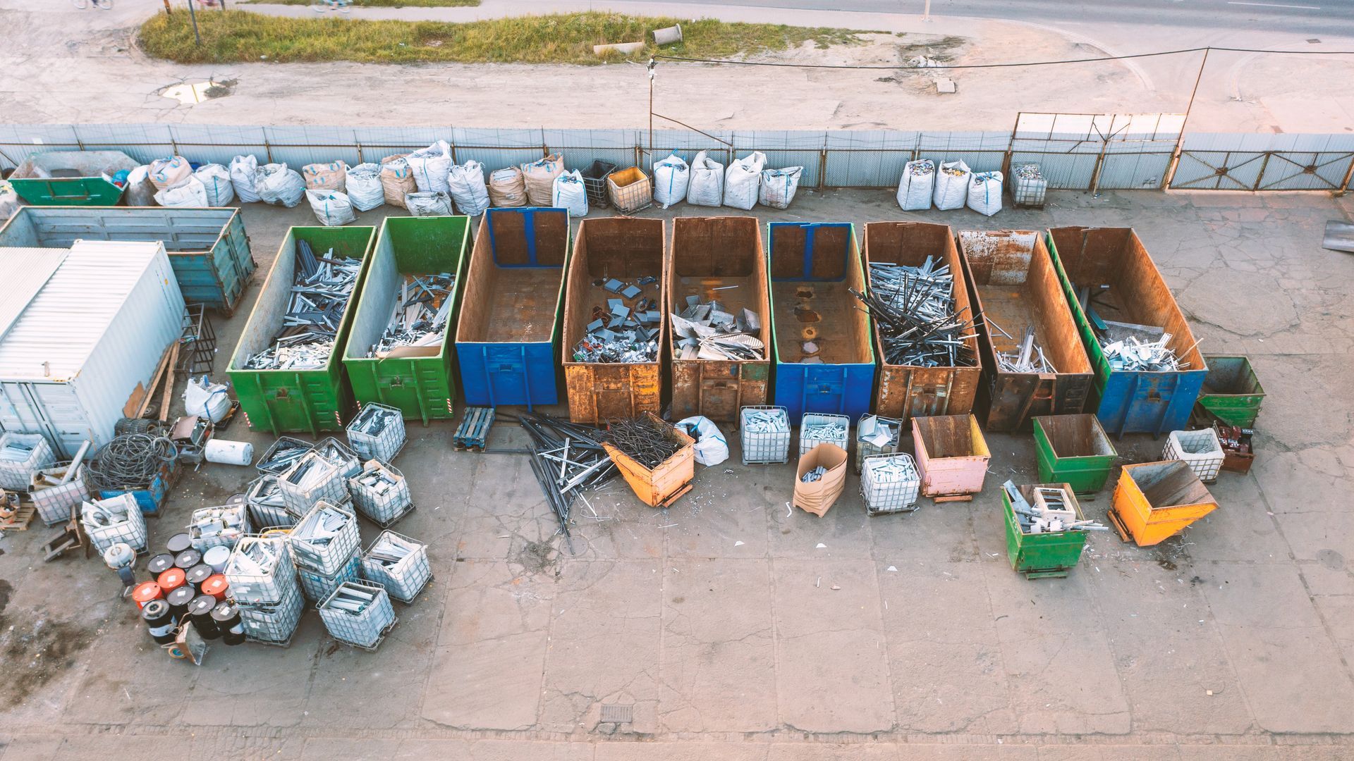 An overhead view of a scrapyard featuring rows of large rectangular containers filled with scrap metal and plastic bags.