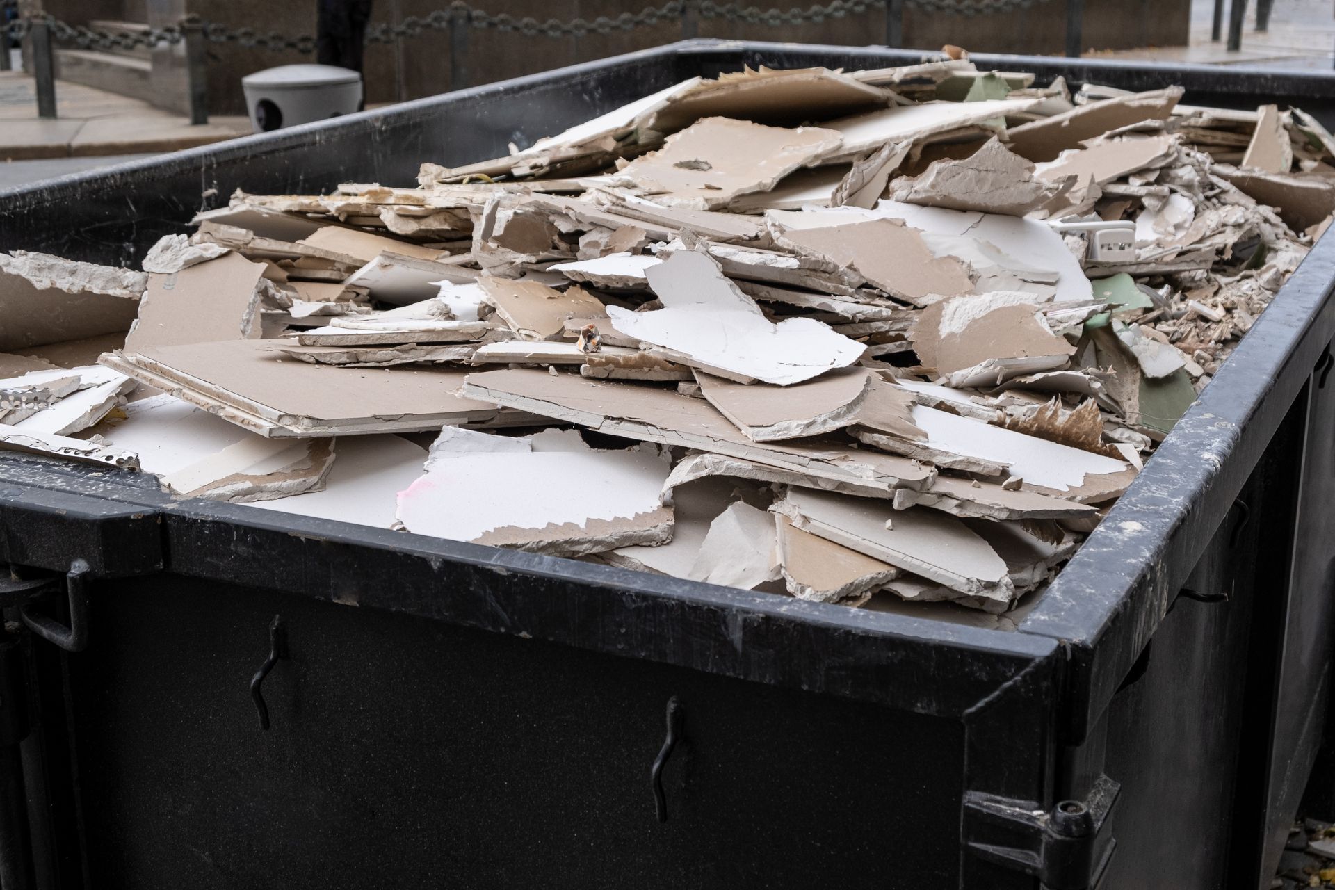 Black dumpster filled with torn drywall pieces.