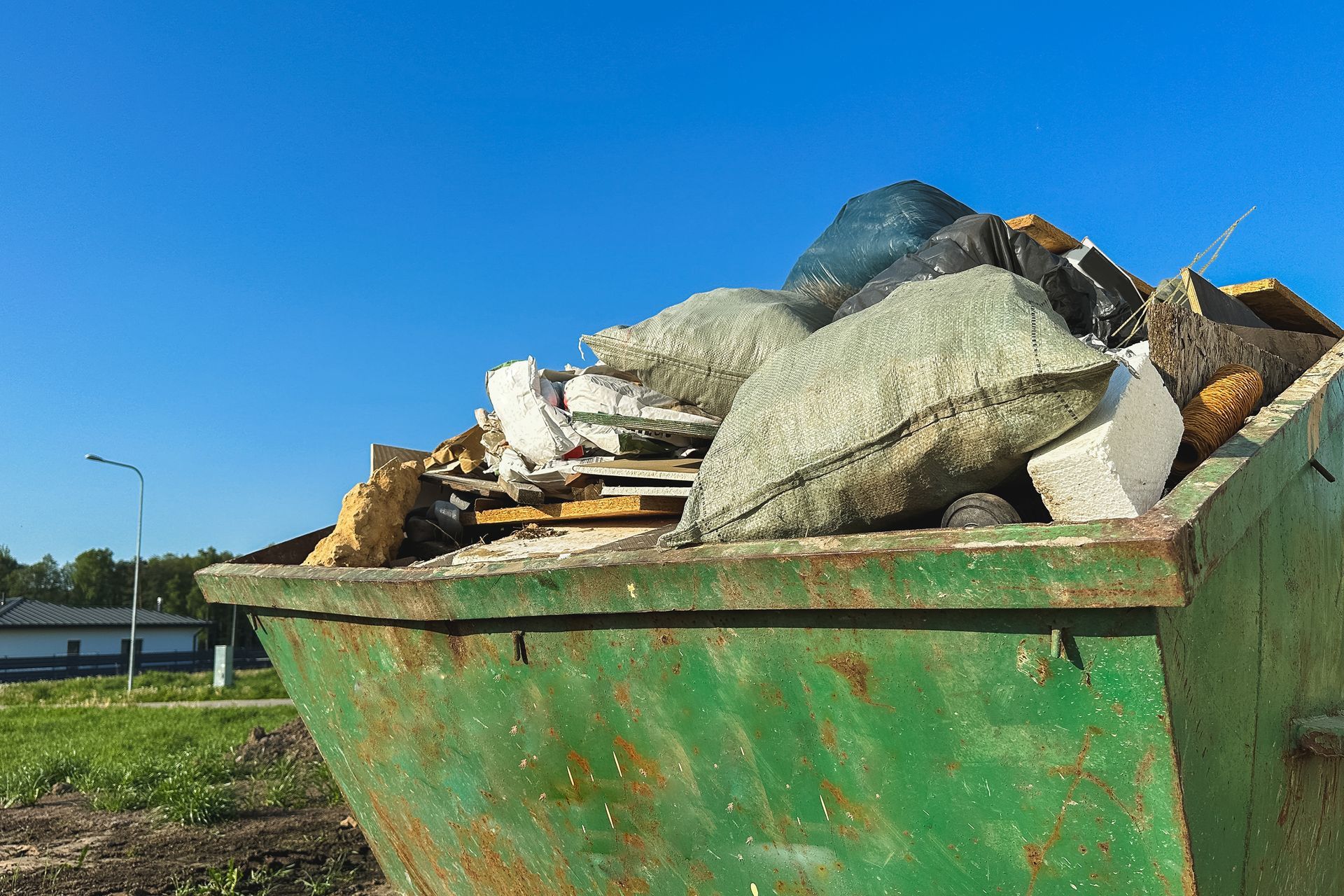 Green dumpster overflowing with construction debris against a blue sky.