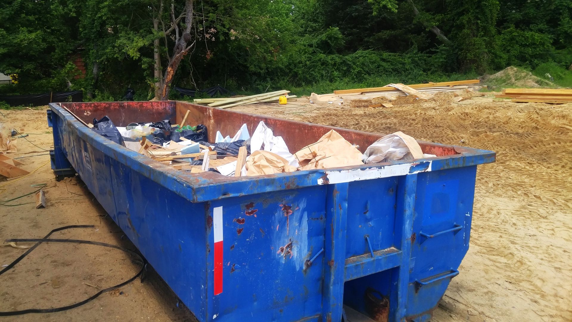 A blue dumpster filled with trash is sitting on top of a dirt field.