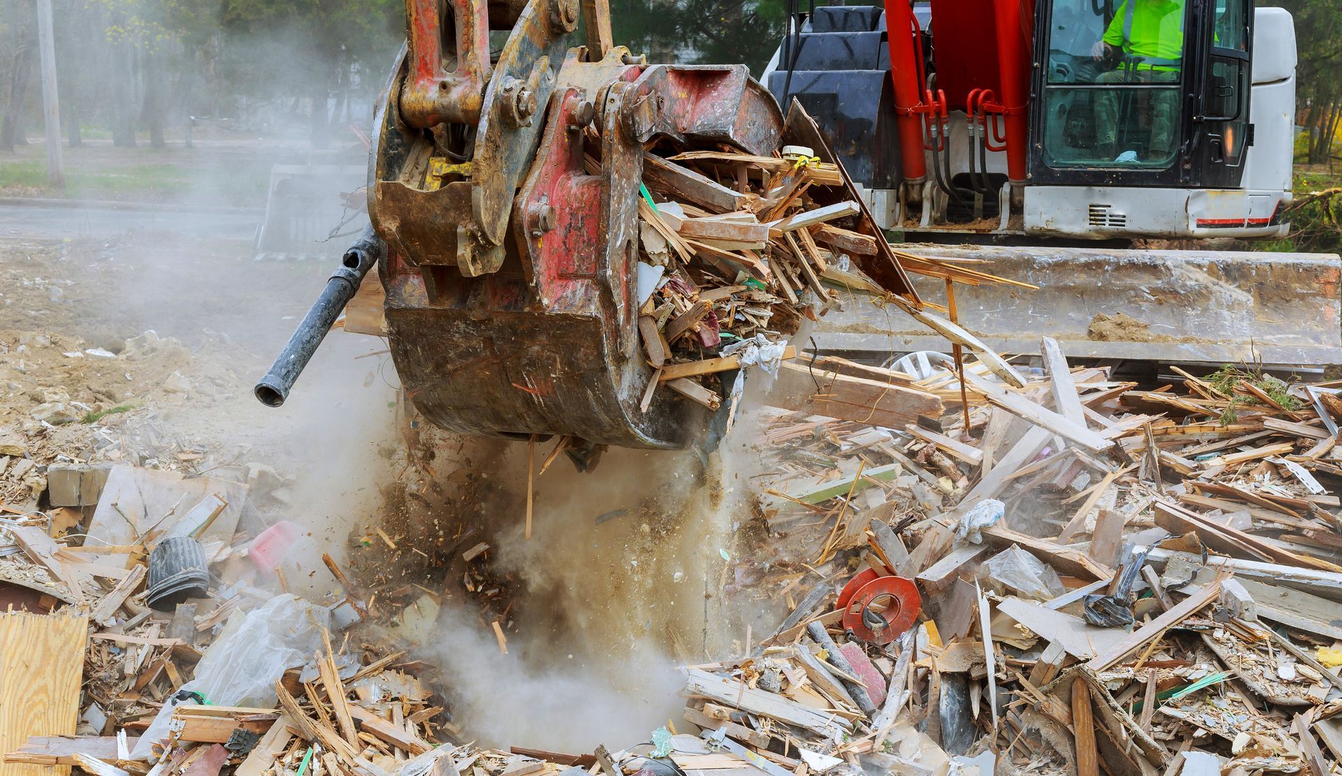 An excavator demolishes debris, with dust and sparks flying. Construction site outdoors.