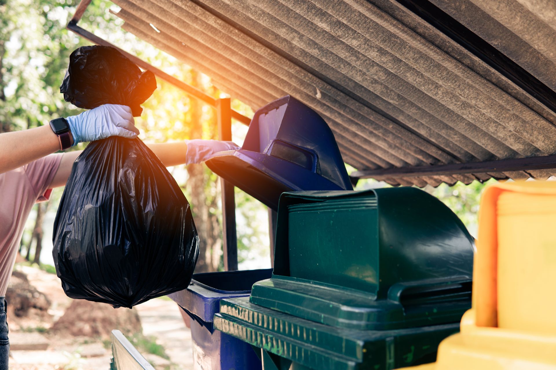 A person is throwing a trash bag into a trash can.