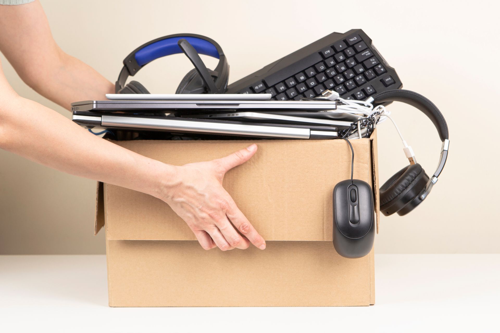 A person is holding a cardboard box filled with computer equipment.