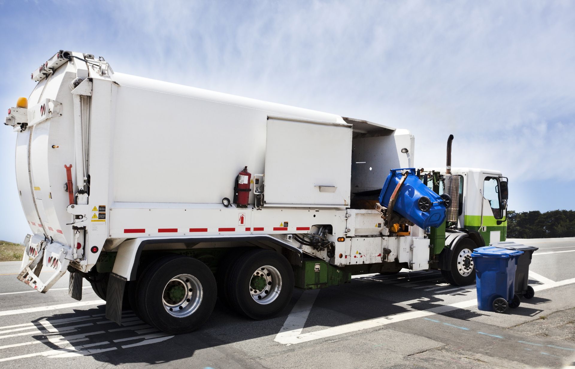 A garbage truck is parked on the side of the road next to a trash can.