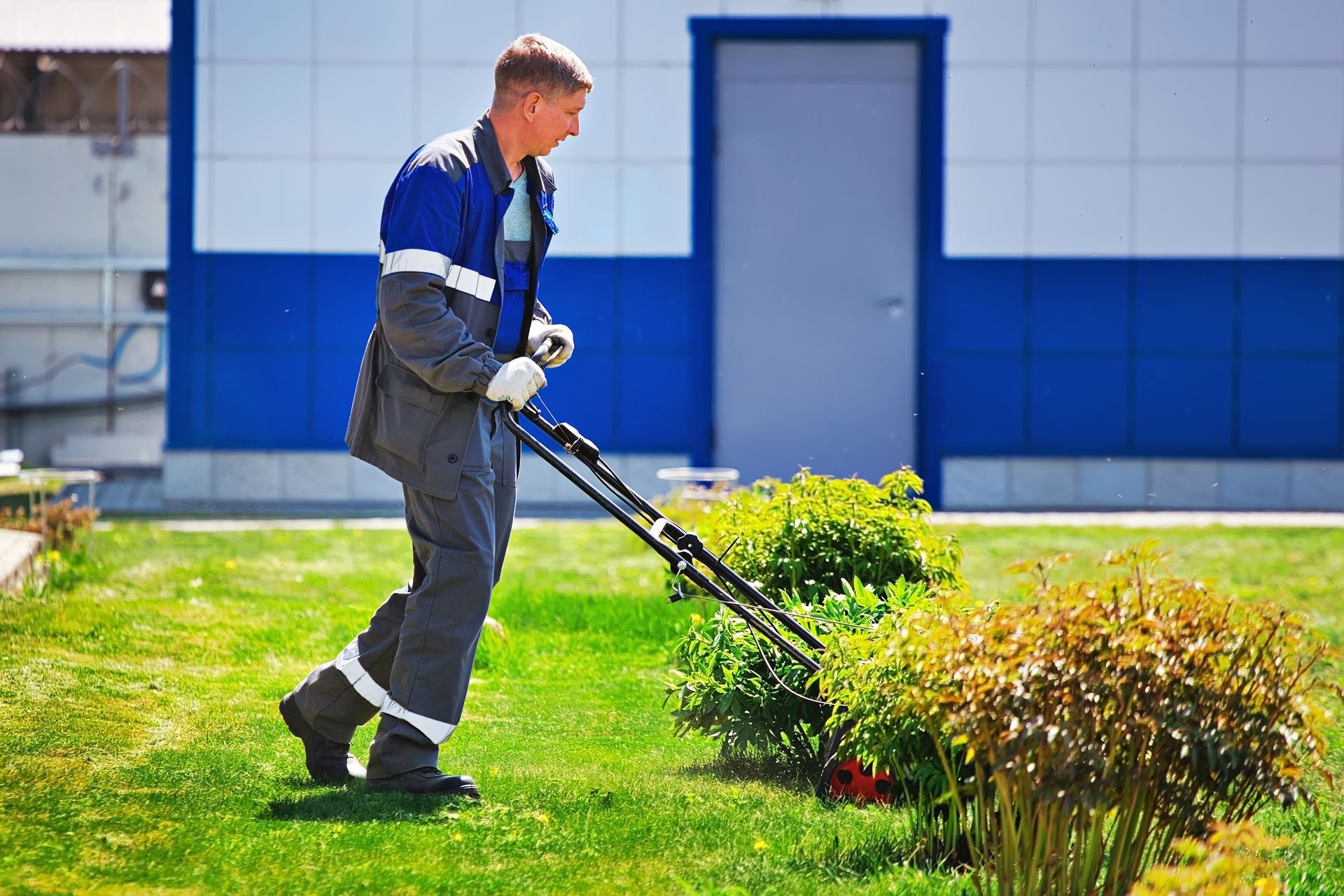 A man is cutting grass with a lawn mower in front of a building.