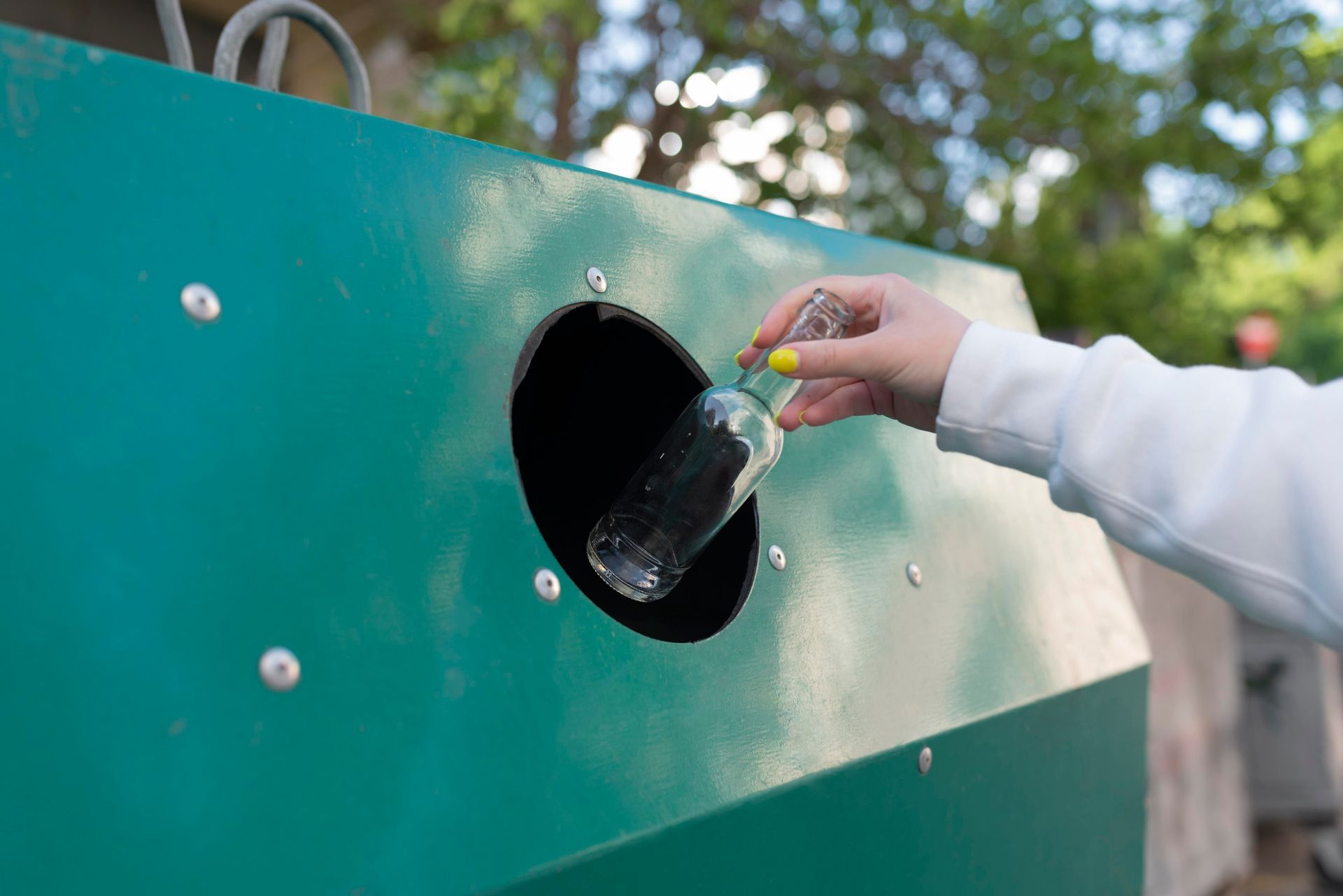 A person is throwing a plastic bottle into a recycling bin.