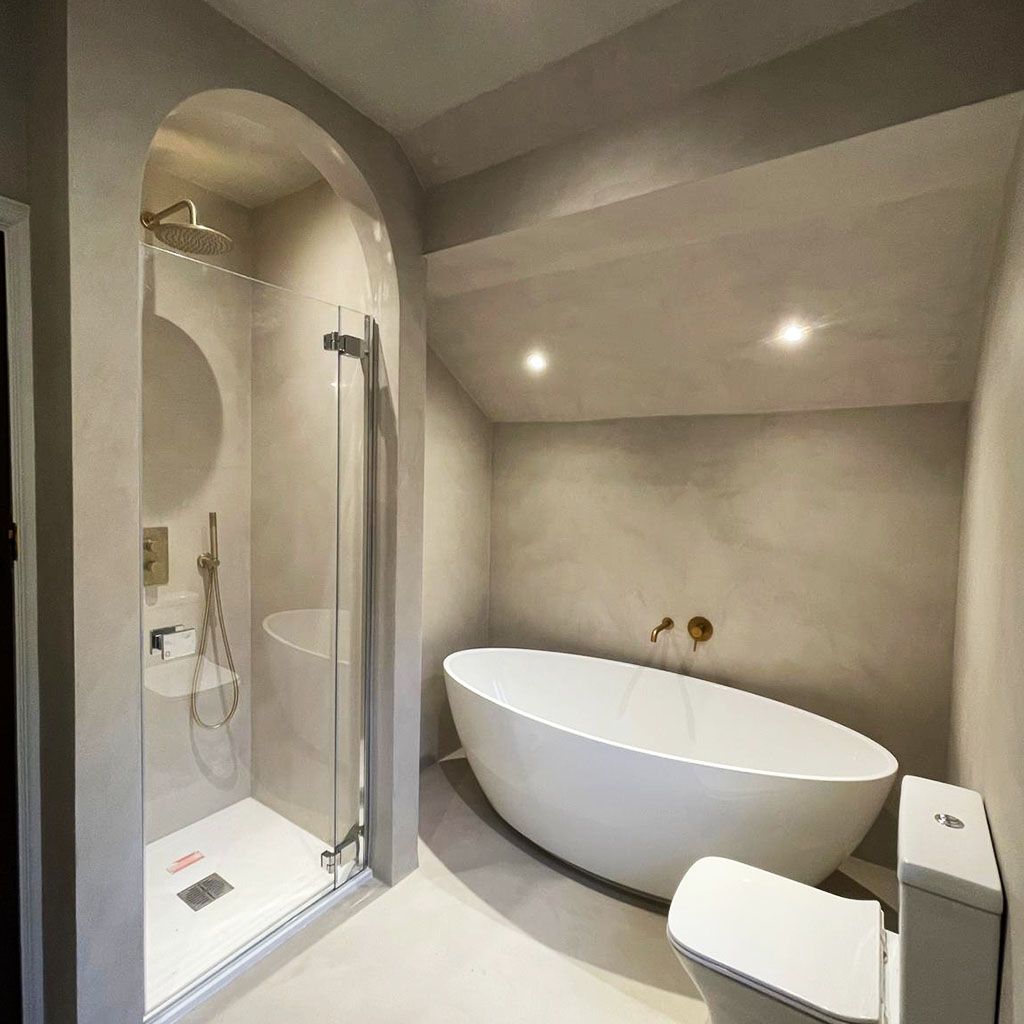 A bathroom with a bathtub, toilet, and shower with microcement walls and floor