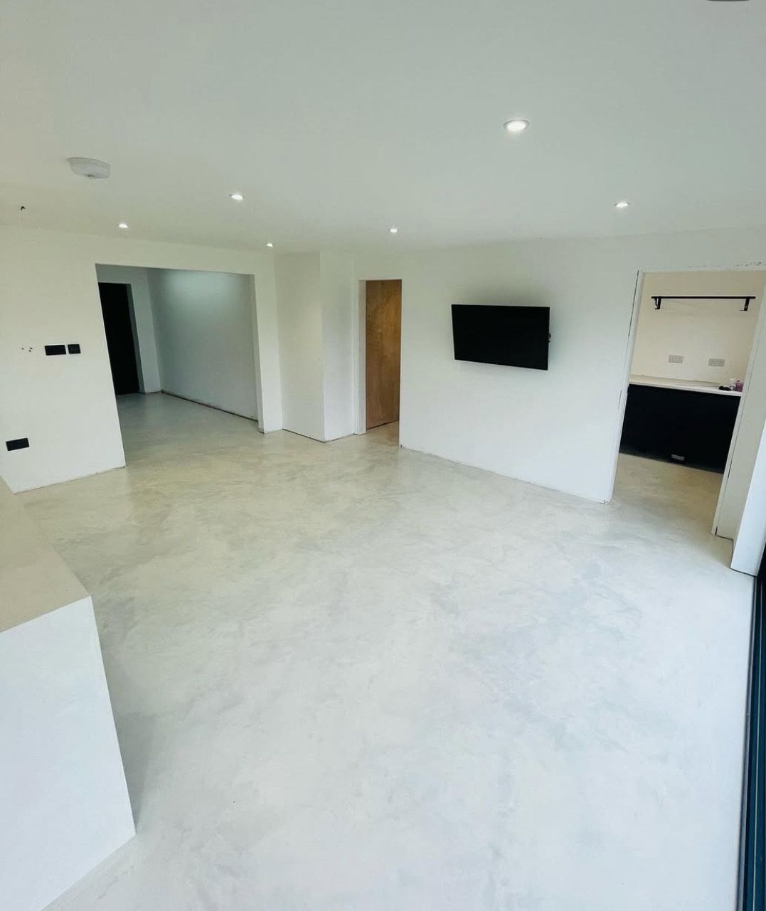 A living room with a flat screen TV on the wall and a microcement floor