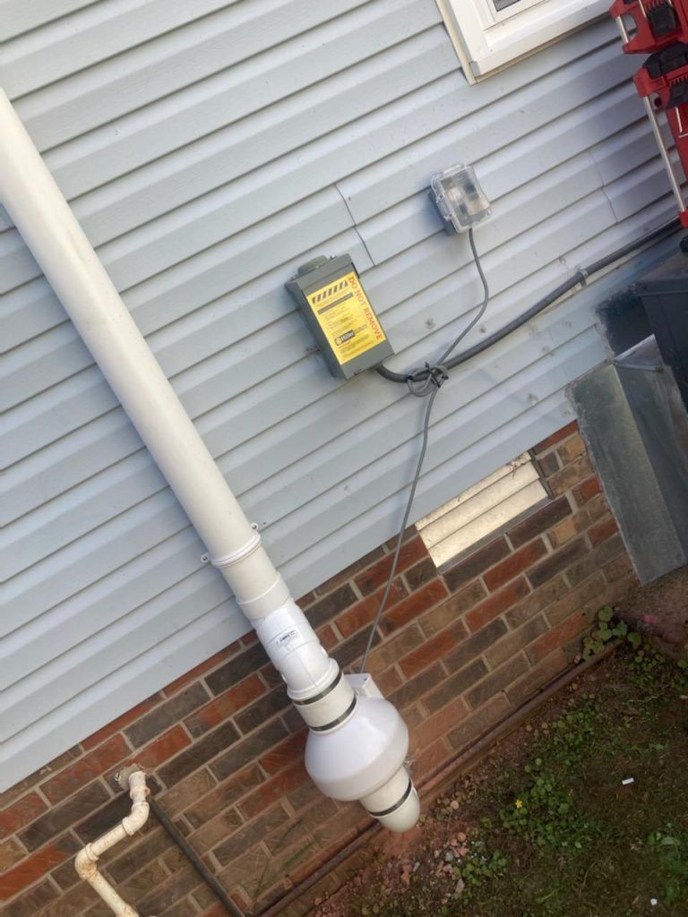 A white pipe is attached to the side of a brick house.