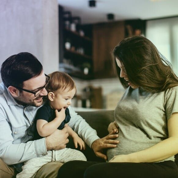 A man and woman are sitting on a couch with a baby and a pregnant woman