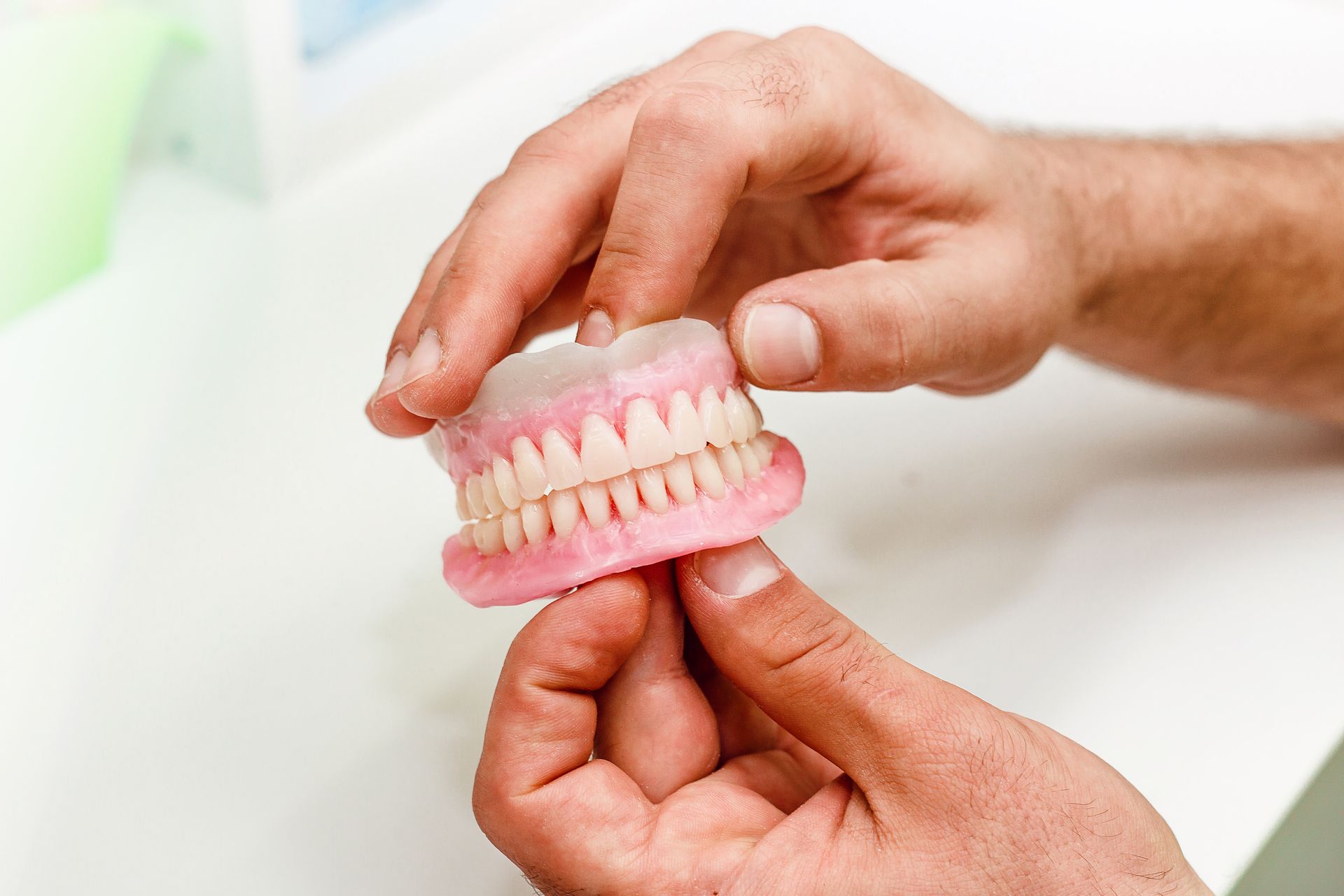 Hands holding a pink dental model with teeth on a white surface