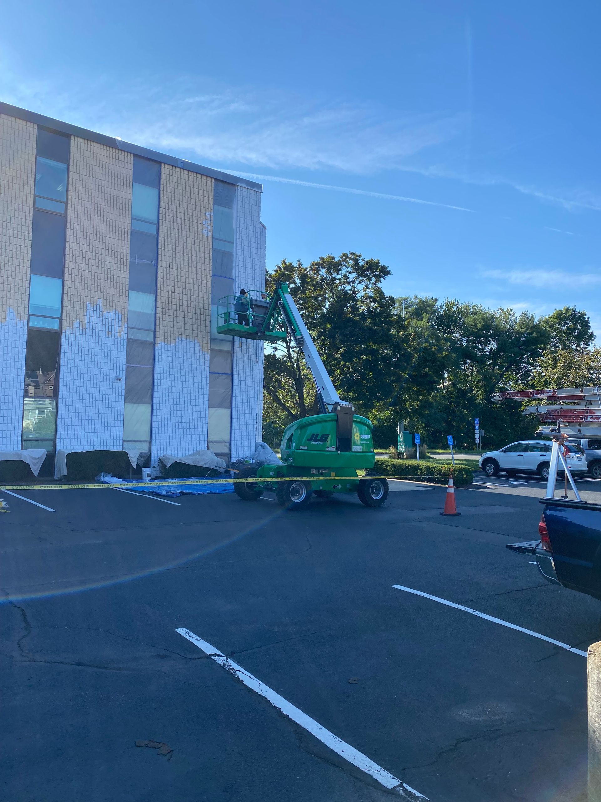 A green crane is working on a building in a parking lot.