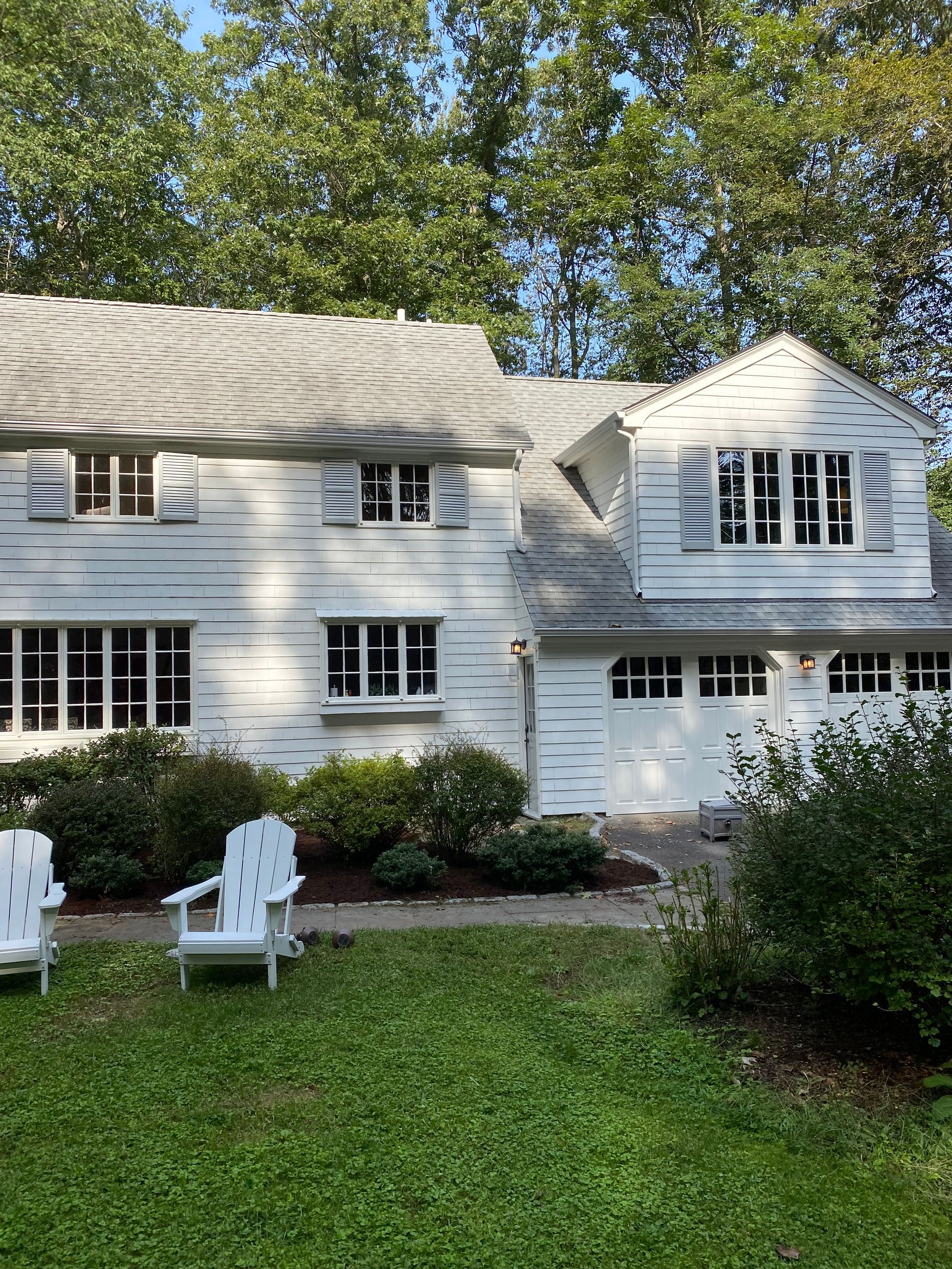 Two white lawn chairs are in front of a white house
