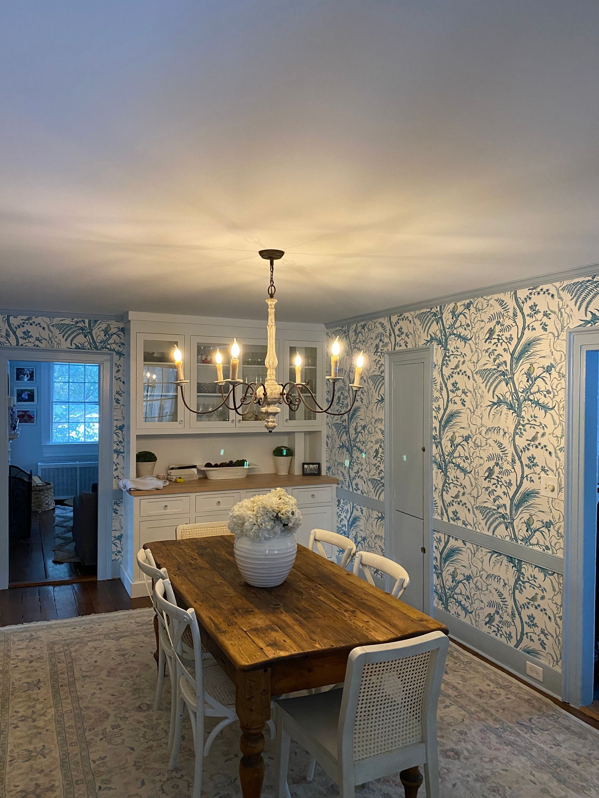 A dining room with a wooden table and chairs and a chandelier hanging from the ceiling.