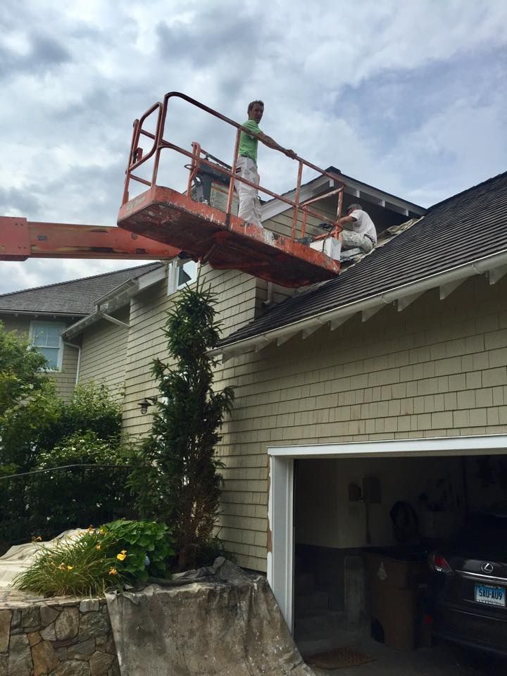 A man is standing on top of a crane painting a house.