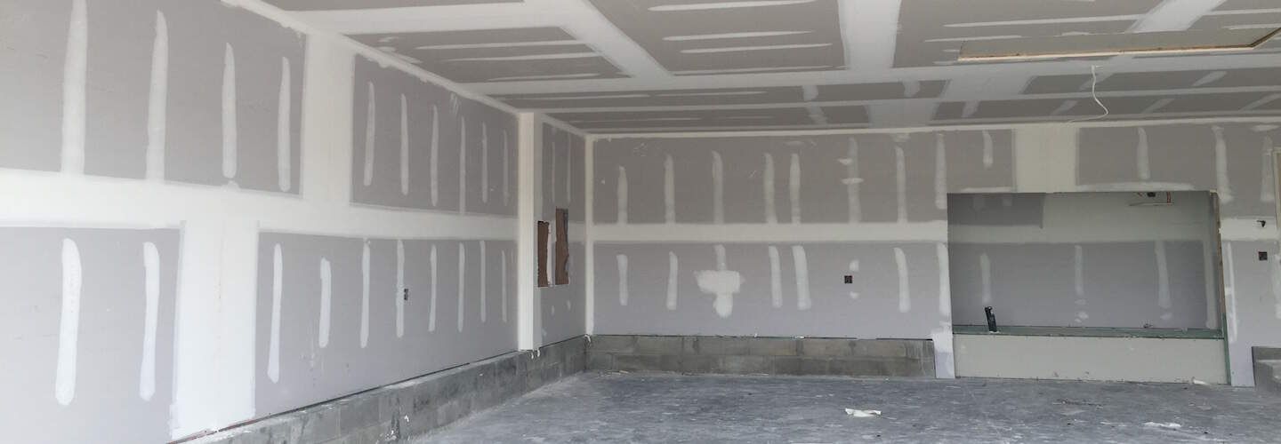 A person is painting a wall with a brush and two cans of paint.