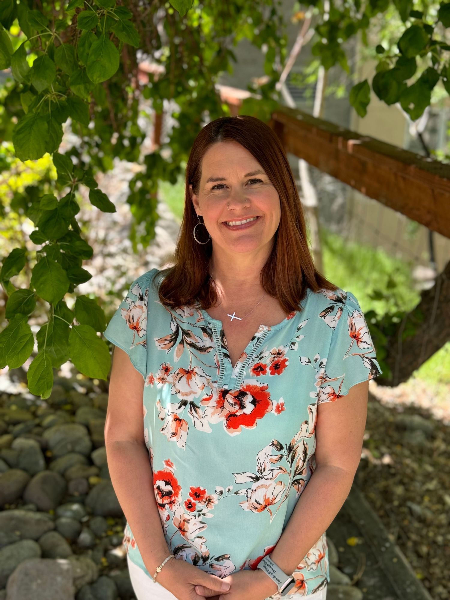 A woman in a blue floral shirt is standing in front of a tree.