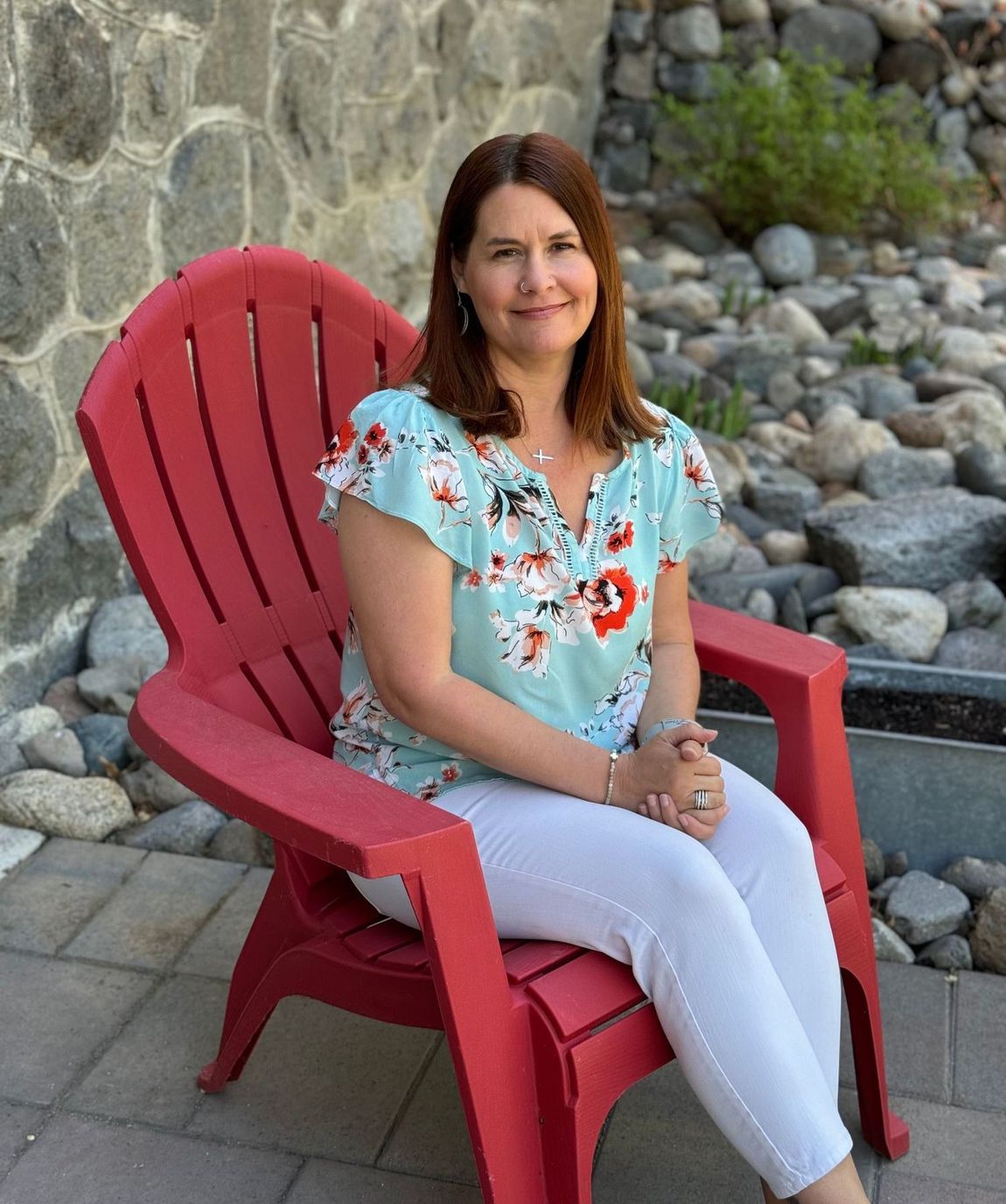 A woman is sitting in a red chair in front of a rock wall.