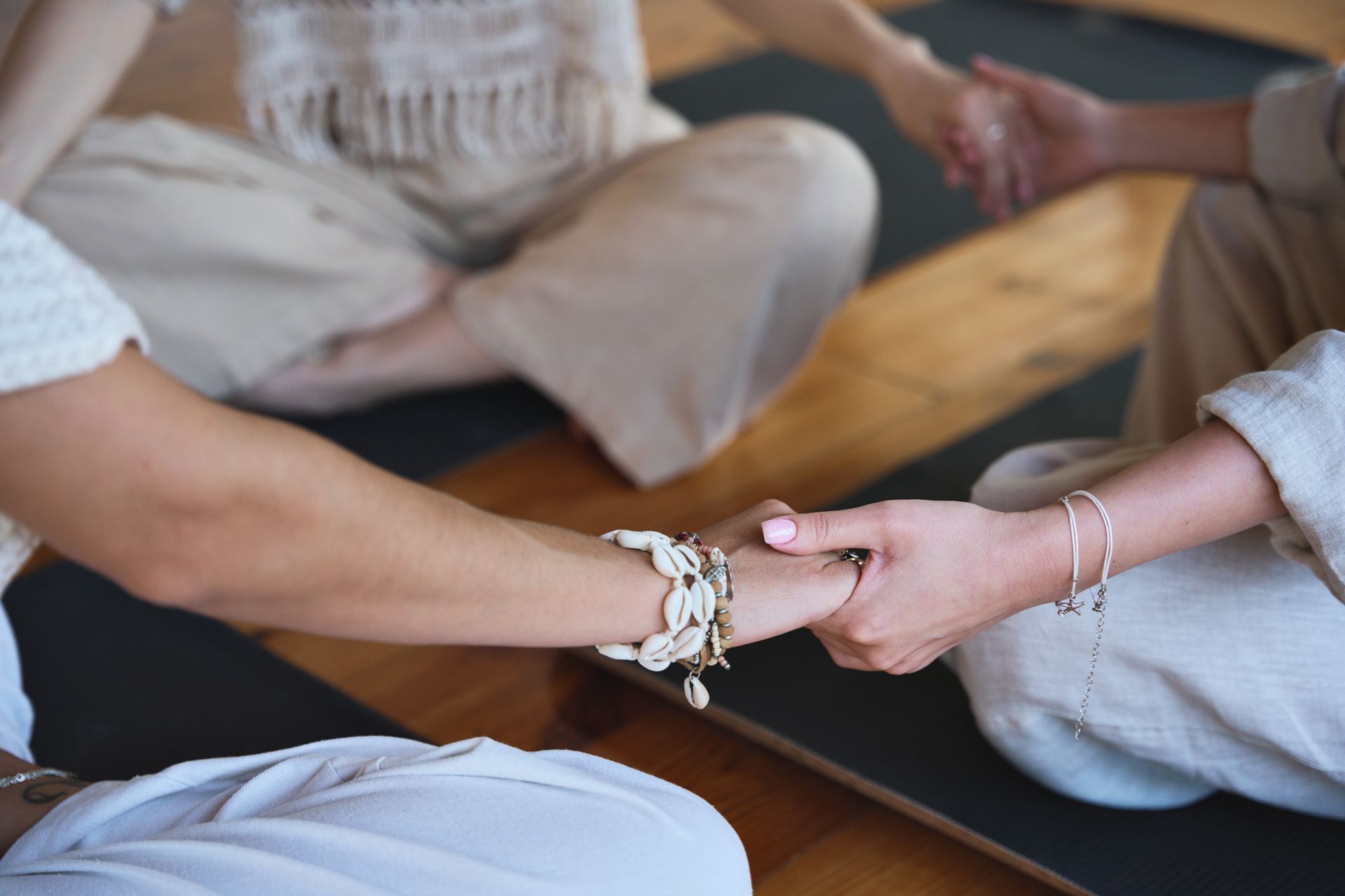 Two people sitting cross-legged on a mat, holding hands in a calm group setting