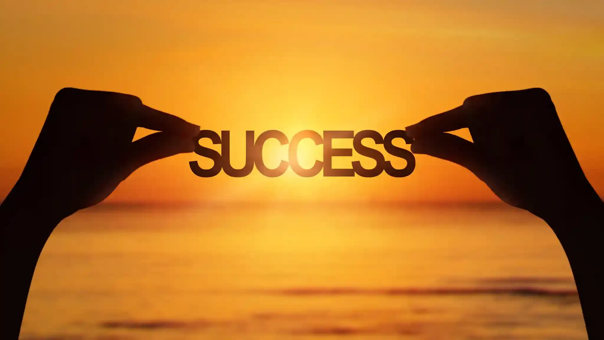 A person is holding the word success in front of a sunset over the ocean.