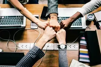 A group of people are putting their fists together on a desk.