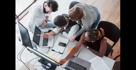 A group of people are sitting around a table looking at a computer screen.
