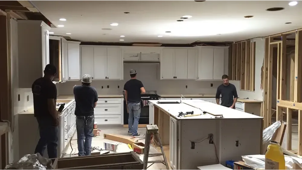 Four men installing white kitchen cabinets in a house under renovation.