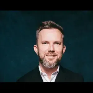 A man with a beard is wearing a suit and smiling.