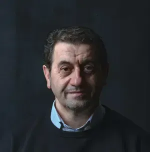 A man with a beard is wearing a black sweater and a blue shirt.