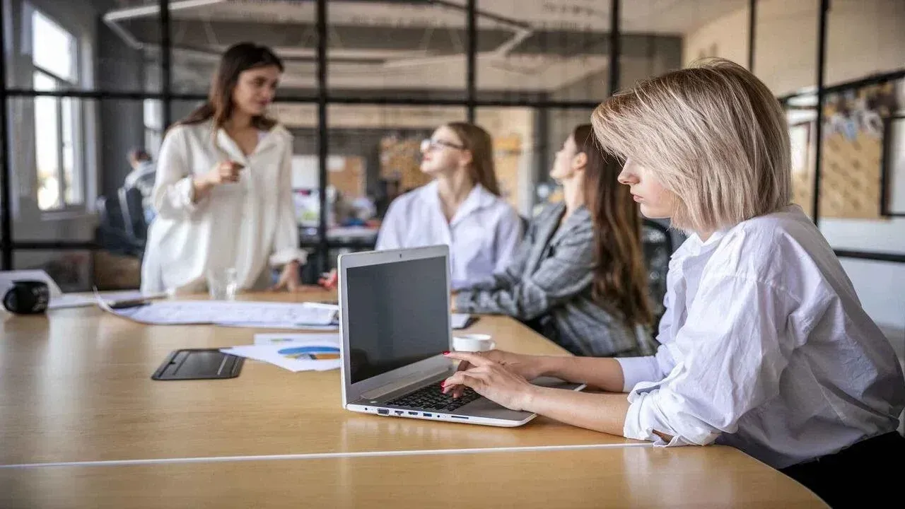 A group of women are sitting at a table with a laptop computer.