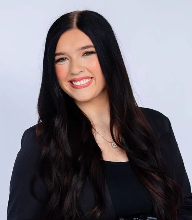 Gracie Watts, Executive Assistant at Beyond Technology, a female with long dark hair smiles while wearing a black blazer and a necklace against a light grey background.